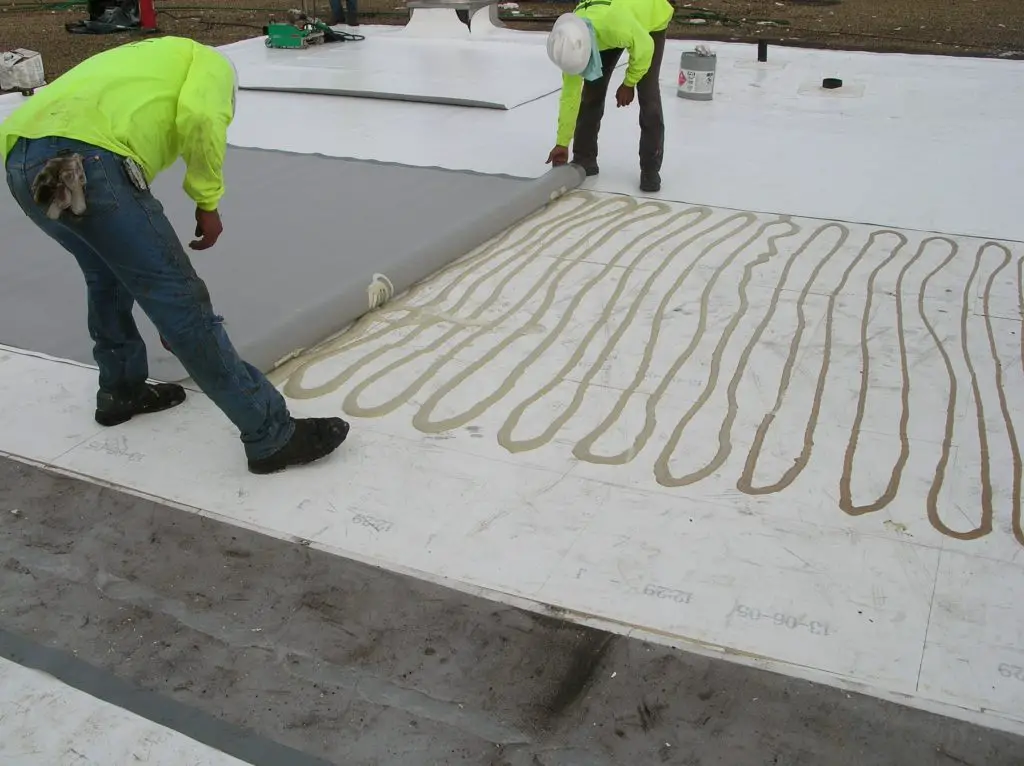 Applying polyurethane roofing adhesive to the cover board before setting a PVC roofing membrane