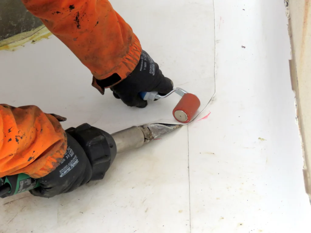 Using a handheld heat gun and a hand roller to apply a TPO patch