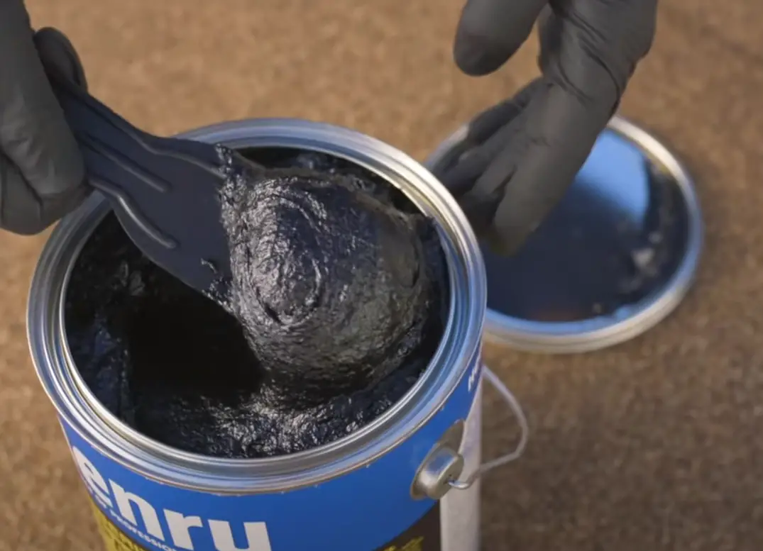 Hand using a plastic tool to use roofing cement. 