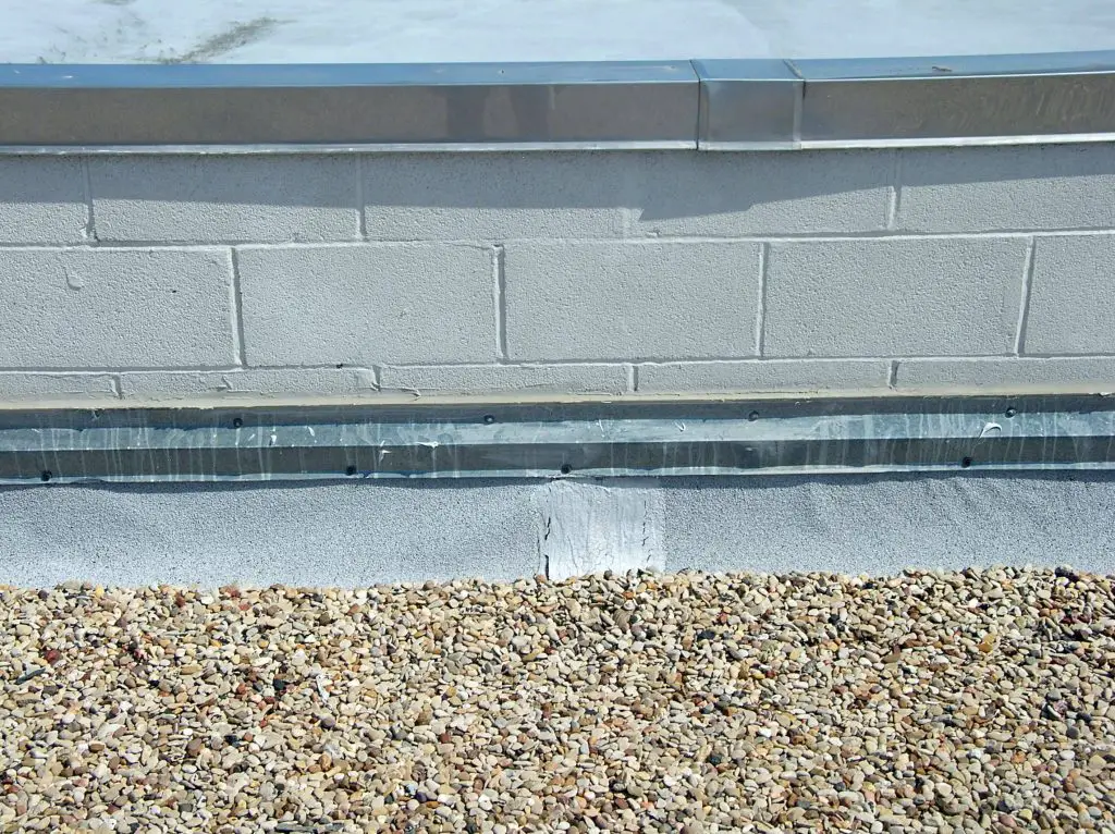 A coated concrete masonry unit parapet wall with stainless steel coping, modified bitumen base flashing, and surface-mounted metal counter-flashing.