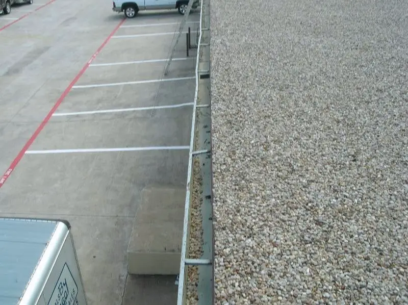 A rain gutter on a gravel-surfaced built-up roof. Removing loose gravel from the gutters is a common maintenance item with this type of roof.