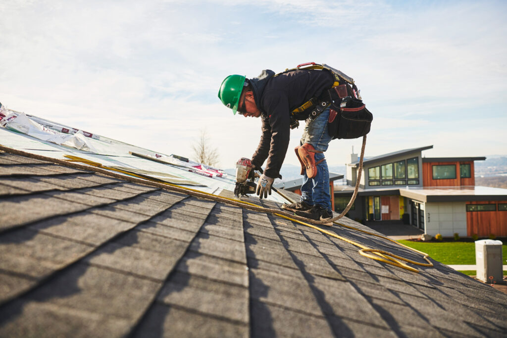 A roofer installing asphalt shingles with an automatic nailer.