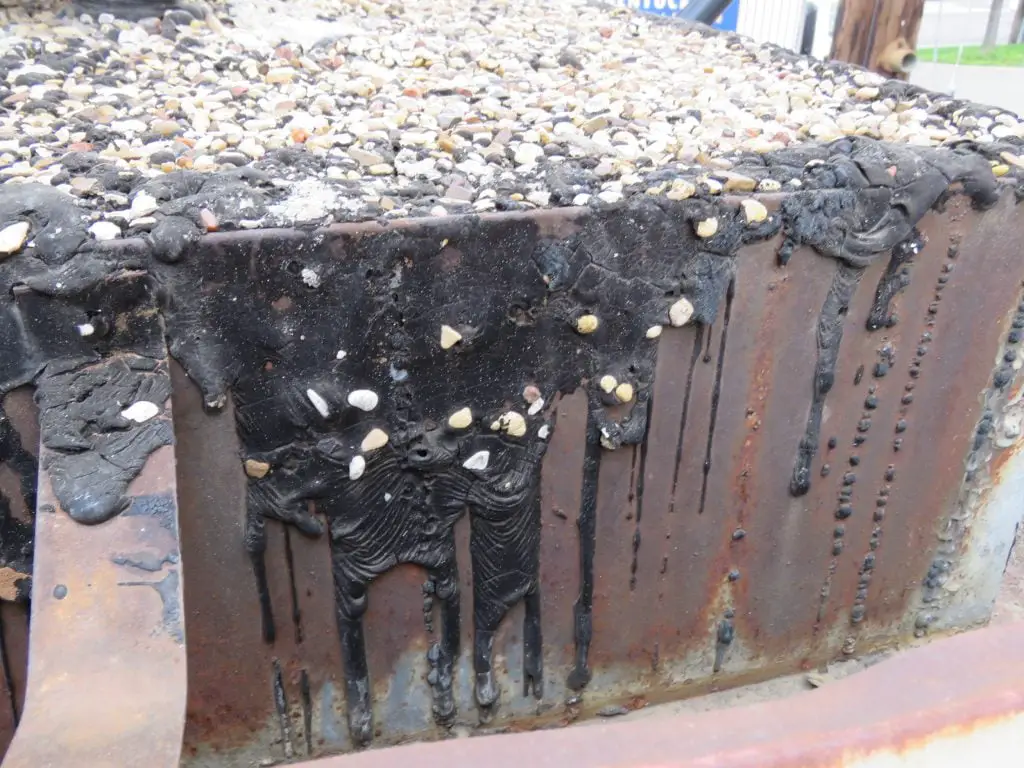 Ripples that have formed in coal tar pitch roofing material on a vertical surface.