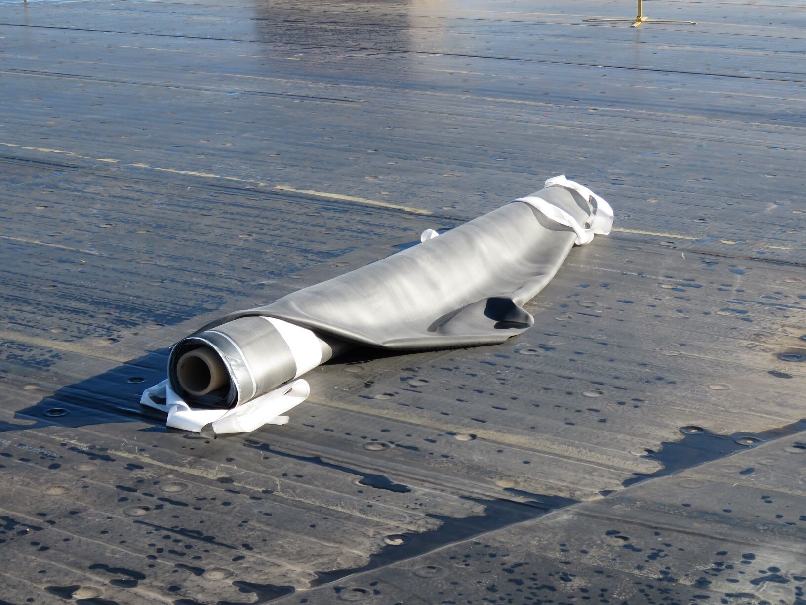 A roll of 10 foot by 100 foot 60-mil EPDM lying on a new EPDM roof.