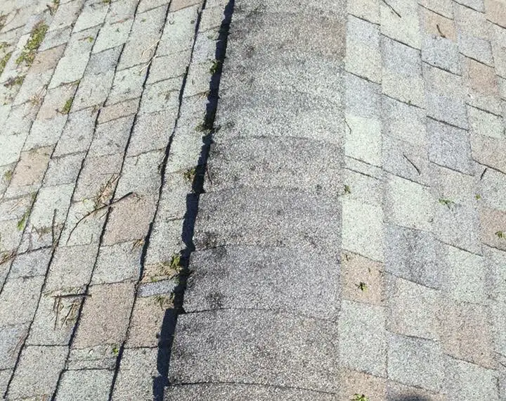 Hail-damaged asphalt shingles. You can see shingles with broken corners, missing ceramic granules at impact points, and wind-blown debris.