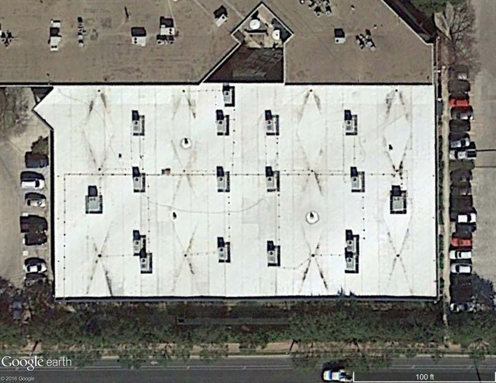 Satellite image of a TPO membrane roof with dirt built up at roof crickets between drains.