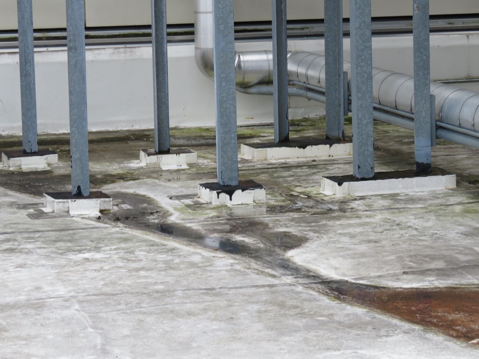 A group of large pitch pans on a PVC roof provide a seal around angled equipment supports.