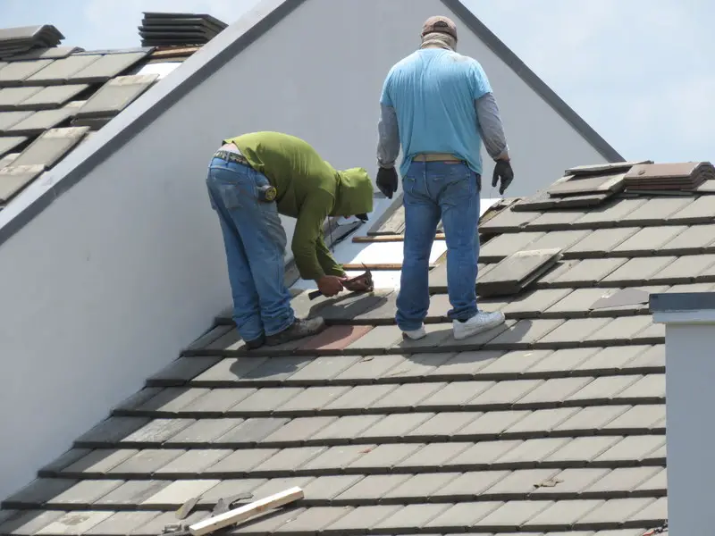 Always check a roofing contractor's license before you hire them. Roofers at work on a tile roof.