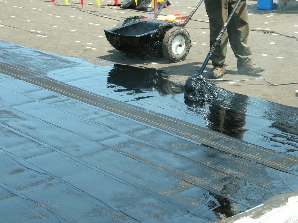 Roofing asphalt being applied to a built-up roof: Hot mopping in the field of the roof.