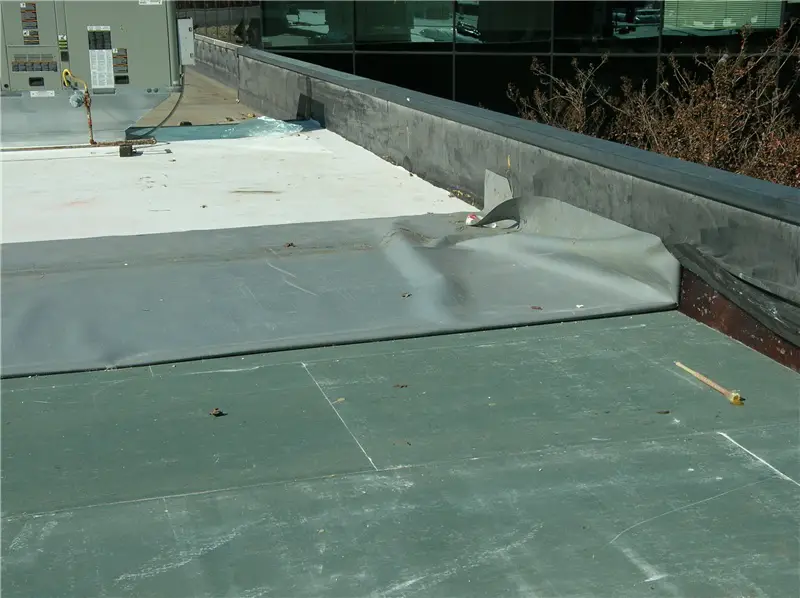 A sheet of TPO during a roof installation, folded back on itself to show the white top surface and the gray underside.