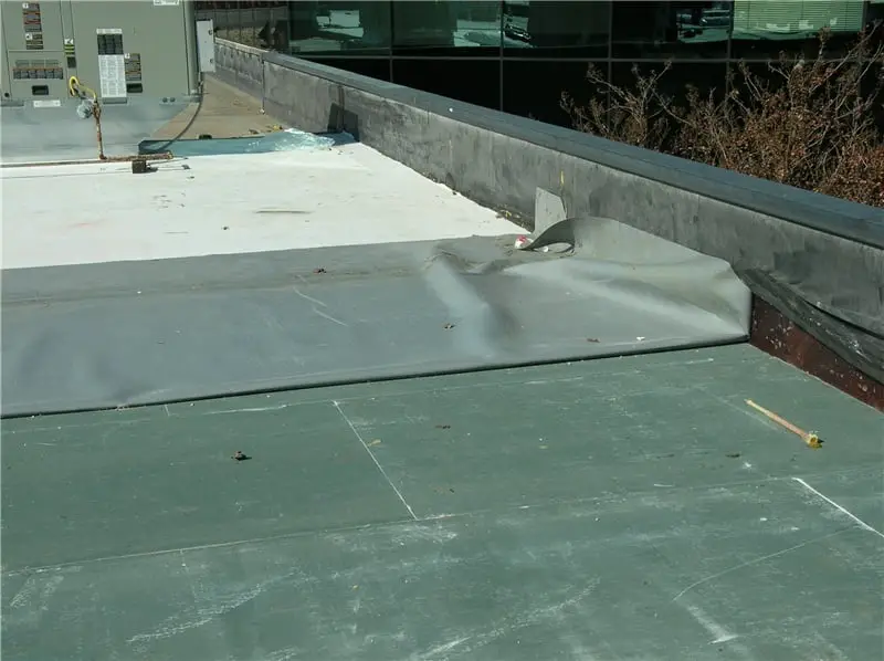 A sheet of TPO during a roof installation, folded back on itself to show the white top surface and the gray underside.