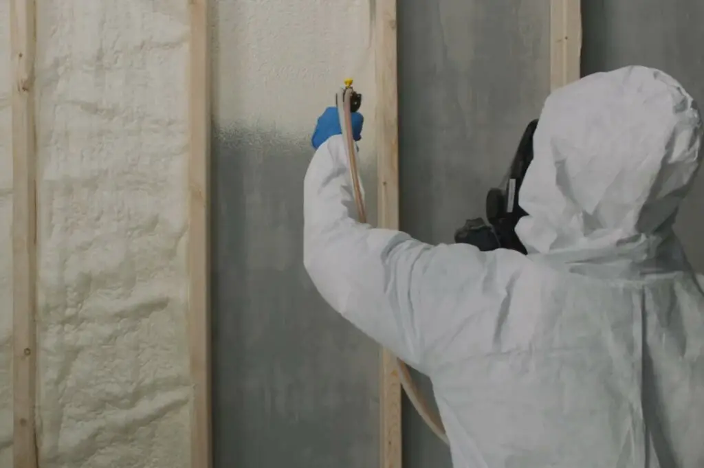 A professional applying spray foam insulation to a basement wall.