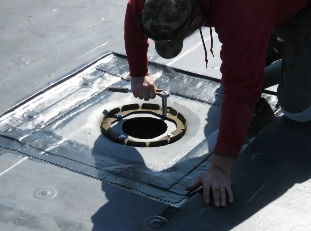 A roofer tightening a roof drain clamping ring bolt.