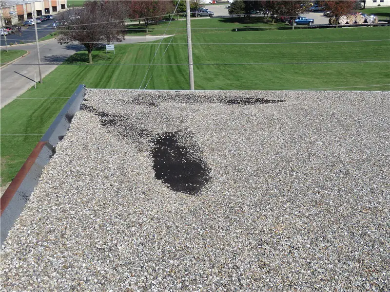 Bare spots in the corner of a built-up roof due to wind scour.