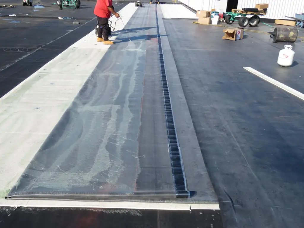 A roofers applying membrane bonding adhesive to a sheet of EPDM during the installation of a fully-adhered EPDM rubber roof.